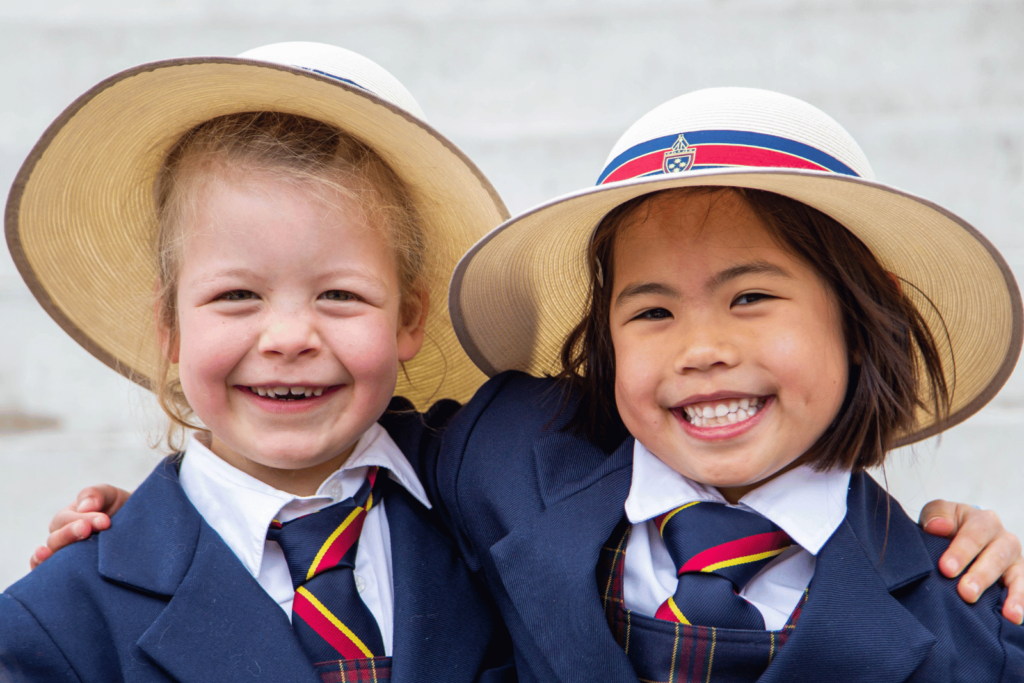 Two young girls in navy school uniforms with ties and hats smile